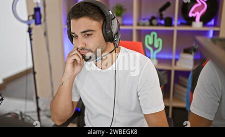 Un giovane concentrato con la barba che indossa cuffie e cuffie in una moderna sala giochi di notte. Foto Stock