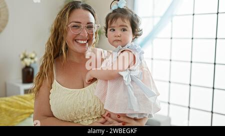 Mamma felice in piedi a casa, tenendo la sua adorabile bambina in braccio, godendo l'amore della famiglia insieme nel loro soggiorno interno con un Foto Stock