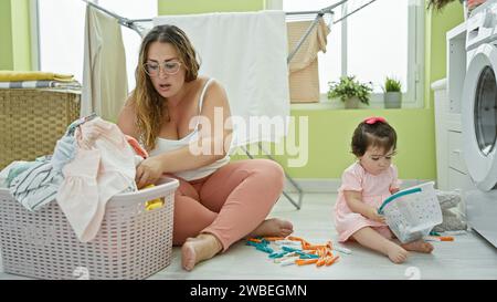 Madre e figlia condividono un momento serio mentre tengono insieme vestiti e un cestino di vimini nell'accogliente lavanderia della famiglia, un angolo della loro vigilia Foto Stock