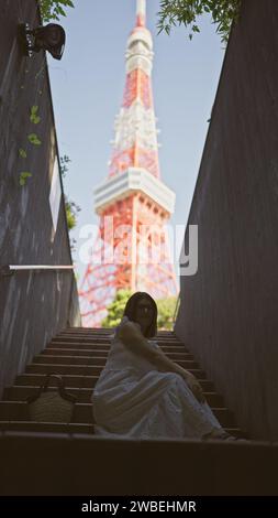 Bellissima donna ispanica con occhiali appollaiati sulle scale, un ritratto della modernità urbana nel famoso punto della torre di tokyo Foto Stock