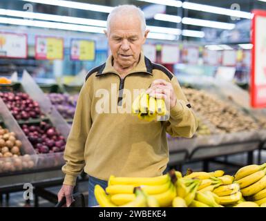 Senor man pensionato che compra banane al supermercato Foto Stock