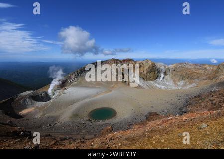 Uno splendido paesaggio naturale caratterizzato da una sorgente termale incastonata in una montagna, circondata da una lussureggiante vegetazione e da un vivace cielo blu Foto Stock