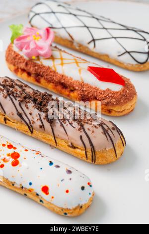 Bellissime e deliziose eclair francesi con decorazioni originali color crema su piatto bianco. Gustosi e colorati dessert profiteroles Foto Stock