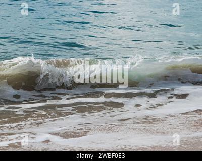 Vista ravvicinata di una piccola onda che si rompe vicino alla spiaggia sabbiosa Foto Stock