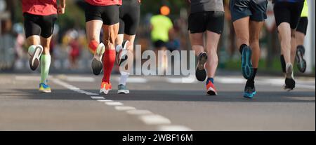 Maratoneti che corrono su strada di città, un grande gruppo di corridori, corridori ravvicinati che corrono maratona sportiva, gara maschile di jogging su strada asfaltata, athlet Foto Stock