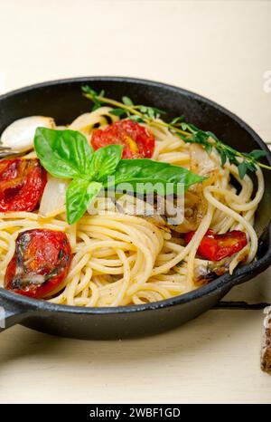 Primo piano degli spaghetti cotti con pomodori ciliegini arrostiti, aglio e basilico fresco Foto Stock