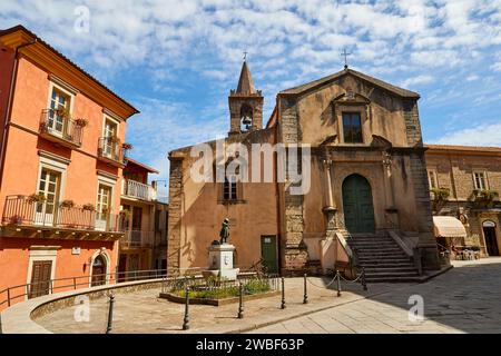 Una piccola piazza con un'antica chiesa e statue sotto un cielo blu in una città, Novara di Sicilia, Sicilia, Italia Foto Stock