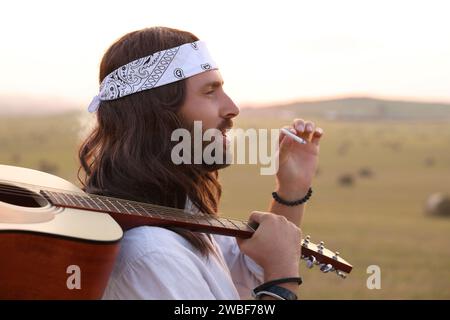 Elegante uomo hippie con fumante chitarra in campo Foto Stock