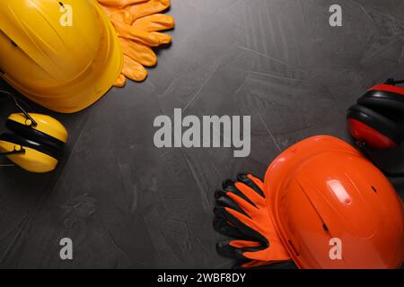 Cappelli rigidi, guanti e cuffie su tavolo grigio, spianati con spazio per il testo. Attrezzatura di sicurezza Foto Stock