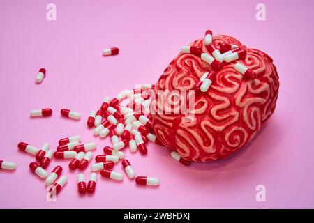 Cervello umano rosso con una pila di pillole e capsule rosse e bianche su un tavolo rosa. Foto Stock