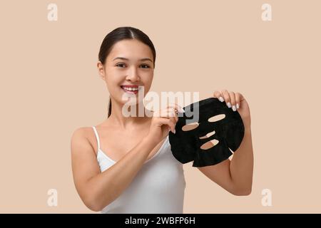 Giovane donna con maschera al carbone attivo su sfondo beige Foto Stock