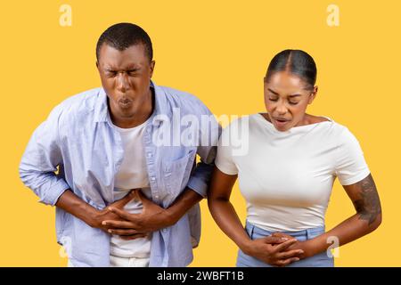 Coppia afroamericana con dolore allo stomaco, espressioni scomode, sfondo giallo Foto Stock