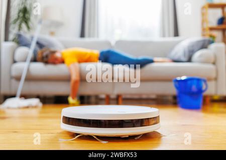 Piano di pulizia con aspirapolvere robot mentre la donna riposa Foto Stock