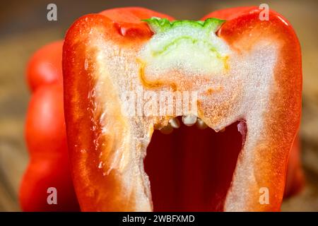 Peperoni rossi interi naturali e freschi, tagliati a metà su una tavola di legno. Foto Stock