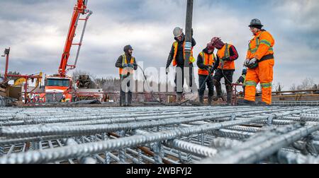 Rouyn-Noranda, Quebec, Canada, 2022-11-25, lavoratori che costruiscono una lastra di cemento per un ponte durante l'inverno, utilizzando una pompa per calcestruzzo Foto Stock