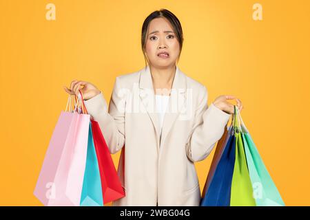 Triste confuso giovane donna cinese che fa shopping con borse colorate, con acquisti Foto Stock