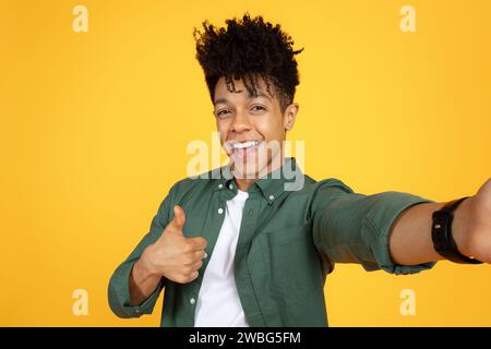 Un giovane ragazzo nero positivo che fa selfie su sfondo giallo Foto Stock