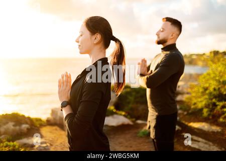 Uomo e donna sereni che praticano la meditazione all'aperto al tramonto Foto Stock