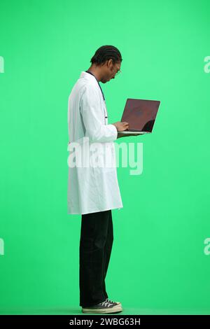 Un medico di sesso maschile, su sfondo verde, a piena altezza, utilizza un notebook Foto Stock