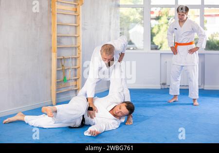 Lezioni di judo o jiu jitsu - due uomini di età diversa che praticano la presa e il lancio su tappetini sportivi Foto Stock