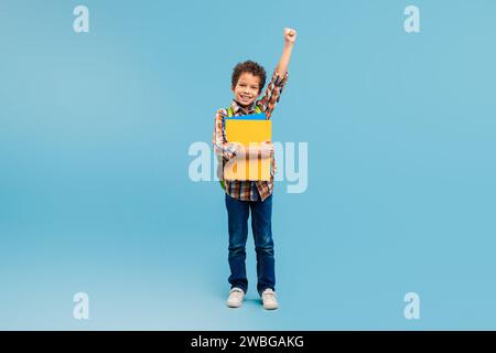 Esuberante scolaro con il pugno in alto, con la cartella in mano, pronto per la scuola Foto Stock