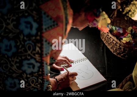 donna non identificabile che scrive e disegna un cuore in un quaderno Foto Stock