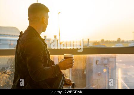 Un giovane che tiene una tazza di caffè è pronto per salire a bordo con la sua valigia. Foto Stock