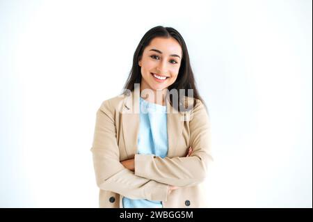Ritratto di una donna d'affari indiana o araba di successo, dirigente, designer, vestita in elegante abito, si erge su uno sfondo bianco isolato con le braccia incrociate, guardando la fotocamera e sorridendo Foto Stock