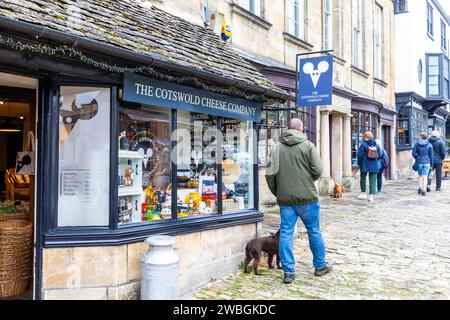 Burford, nel Cotswolds, il negozio di formaggi Cotswold e l'uomo che passeggia con il suo cane, Inghilterra, Regno Unito, 2023 Foto Stock