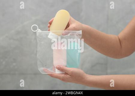 Donna che indossa kit da viaggio cosmetico vicino a una parete grigia per primo piano. Accessori per il bagno Foto Stock