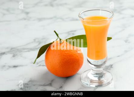 Delizioso liquore al mandarino in bicchierino e frutta fresca su un tavolo in marmo bianco, primo piano Foto Stock