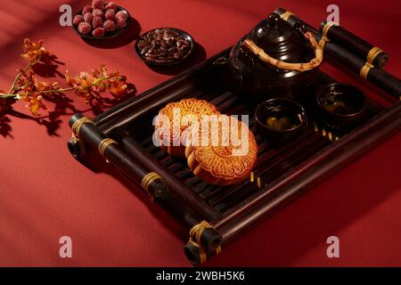 Un vassoio presentava due torte lunari e un set da tè disposti su sfondo rosso con piatti di marmellata caramelle e semi di melone. Mooncake per il Mid-Autumn Festival Holi Foto Stock