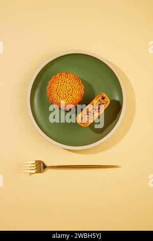 Sullo sfondo pastello, un piatto verde comprendeva una torta di luna e una mezza torta di luna. Una forchetta dorata. Le usanze di celebrare il Mid-Au Foto Stock