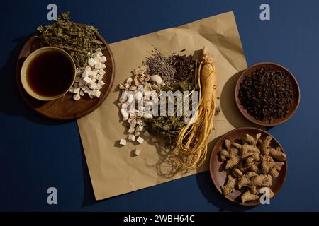 Su una carta sono presenti radici di ginseng, foglie di menta secca, lavanda e zenzero di sabbia. Altra medicina con una ciotola di tonico in giro Foto Stock