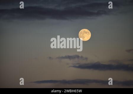 La luna piena emette un soffice bagliore giallastro in un cielo al crepuscolo con un assortimento di nuvole intorno ad esso Foto Stock