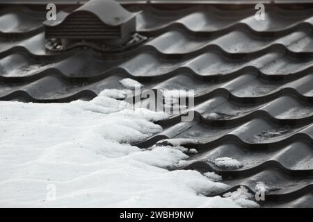 Tetto in metallo nero con piastrelle di neve, foto invernale ravvicinata del tetto di una moderna casa di campagna Foto Stock