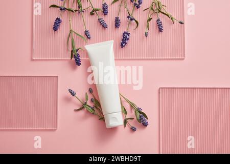 Scena minimalista astratta per la pubblicità e il branding di prodotti con ingredienti di lavanda. Sullo sfondo rosa, un tubo di plastica bianco decorato con f Foto Stock