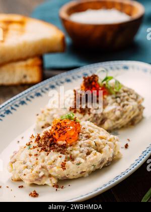 Forshmak antipasto di pesce - carne macinata di pesce aringhe, caviale decorato sul piatto. Piatto tradizionale della cucina ebraica vorschmack forshmak fatto di filetto di aringa come piatto indipendente su sfondo di legno Foto Stock