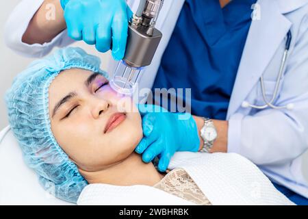 Dottore asiatico che fa laser sulla faccia della donna alla clinica di bellezza. Bella donna con trattamento viso per la cura della pelle presso la clinica di bellezza, trattamento viso anti-invecchiamento Foto Stock