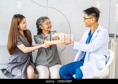 Medico di sesso maschile che insegna fisioterapia al paziente adulto anziano asiatico e figlia in ospedale, per raccogliere informazioni per la terapia fisica trattata Foto Stock