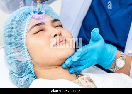 Dottore asiatico che fa laser sulla faccia della donna alla clinica di bellezza. Bella donna con trattamento viso per la cura della pelle presso la clinica di bellezza, trattamento viso anti-invecchiamento Foto Stock