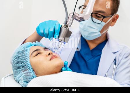 Dottore asiatico che fa laser sulla faccia della donna alla clinica di bellezza. Bella donna con trattamento viso per la cura della pelle presso la clinica di bellezza, trattamento viso anti-invecchiamento Foto Stock