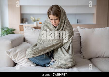 Donna depressa e depressa che piange seduta con gli occhi chiusi avvolta a quadri. Influenza, stagione covid Foto Stock