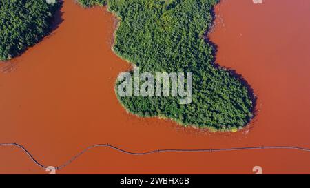 Lago rosso e foresta verde. Bacino di raccolta residui di scarto. Lago inquinato nella natura. Impatto ambientale della produzione di alluminio. Stagno di scarico. Residuo di bauxite. Foto Stock