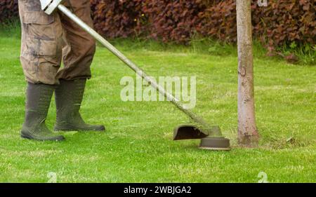 Il giardiniere taglia un prato verde con un rasaerba manuale. Primo piano. Foto Stock