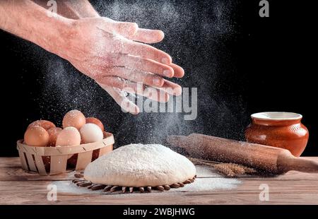 Il fornaio batte le mani con la farina sull'impasto. Un uomo sta preparando del pane fatto in casa in cucina. Il concetto di comfort domestico. Cibo sano. Foto Stock