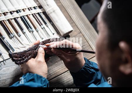 (240111) -- CHONGQING, 11 gennaio 2024 (Xinhua) -- Yu Dahong incide su un pettine di legno in un laboratorio della fabbrica Tanmujiang a Chongqing, nel sud-ovest della Cina, 5 gennaio 2024. L'artigianato tradizionale con pettine di legno di Tanmujiang, che combina l'abilità della decorazione a colori, dell'incisione, della laccatura e della doratura d'oro, sono stati elencati come patrimonio culturale immateriale del comune di Chongqing. Utilizzando bosso, ebano o legno di sandalo come materiali per intagliare motivi come personaggi, fiori e uccelli sui pettini, l'artigianato ha trasformato l'articolo comune nella vita quotidiana in un'opera d'arte con valori estetici. Foto Stock