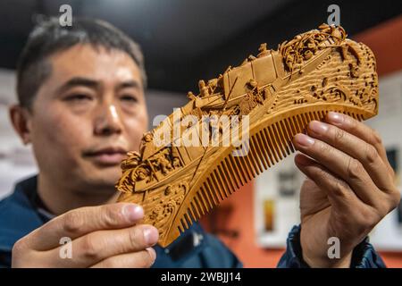 (240111) -- CHONGQING, 11 gennaio 2024 (Xinhua) -- Yu Dahong guarda un pettine di legno che ha inciso in un laboratorio della fabbrica di Tanmujiang a Chongqing, nel sud-ovest della Cina, 5 gennaio 2024. L'artigianato tradizionale con pettine di legno di Tanmujiang, che combina l'abilità della decorazione a colori, dell'incisione, della laccatura e della doratura d'oro, sono stati elencati come patrimonio culturale immateriale del comune di Chongqing. Utilizzando bosso, ebano o legno di sandalo come materiali per intagliare motivi come personaggi, fiori e uccelli sui pettini, l'artigianato ha trasformato l'articolo comune nella vita quotidiana in un'opera d'arte dall'aspetto estetico Foto Stock