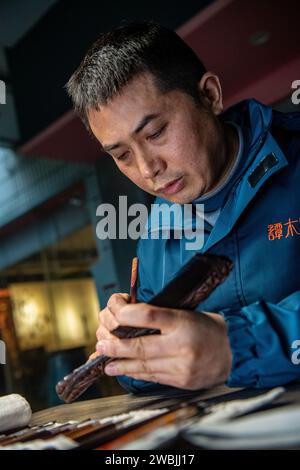 (240111) -- CHONGQING, 11 gennaio 2024 (Xinhua) -- Yu Dahong incide su un pettine di legno in un laboratorio della fabbrica Tanmujiang a Chongqing, nel sud-ovest della Cina, 5 gennaio 2024. L'artigianato tradizionale con pettine di legno di Tanmujiang, che combina l'abilità della decorazione a colori, dell'incisione, della laccatura e della doratura d'oro, sono stati elencati come patrimonio culturale immateriale del comune di Chongqing. Utilizzando bosso, ebano o legno di sandalo come materiali per intagliare motivi come personaggi, fiori e uccelli sui pettini, l'artigianato ha trasformato l'articolo comune nella vita quotidiana in un'opera d'arte con valori estetici. Foto Stock