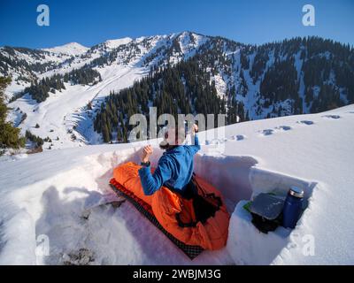 Un viaggiatore con la barba ha passato la notte in un sacco a pelo in un rifugio sulla neve. Viaggiatore mattutino in montagna in inverno Foto Stock